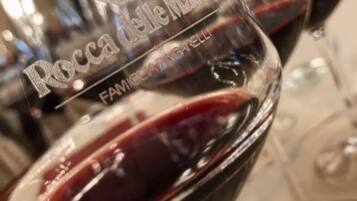 A close-up of a wine glass with the inscription "Rocca delle Marelle" and "FAMIGLIAZIONE".