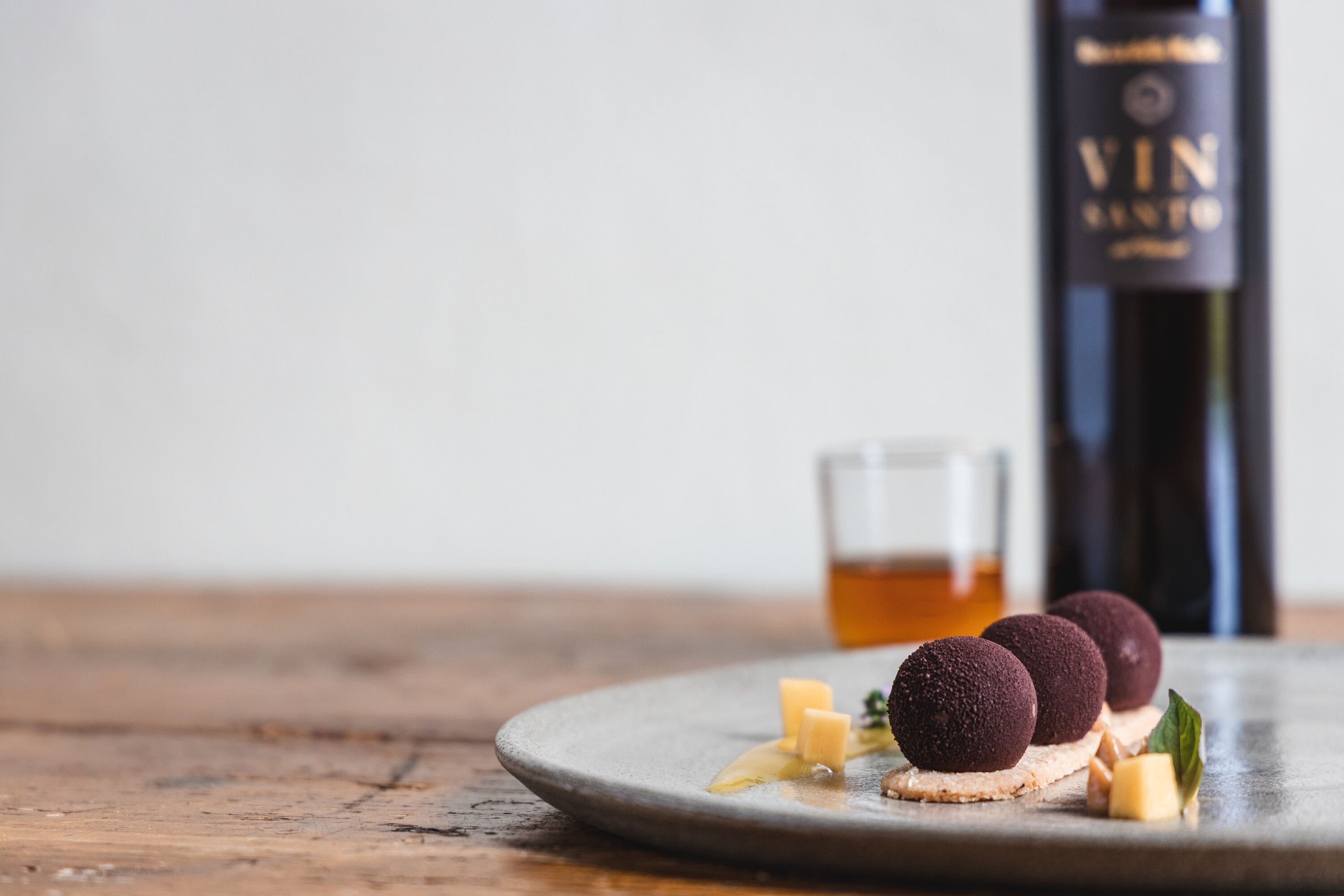 Une assiette avec trois boules de couleur foncée et, en arrière-plan, une bouteille portant l’étiquette « VIN ».