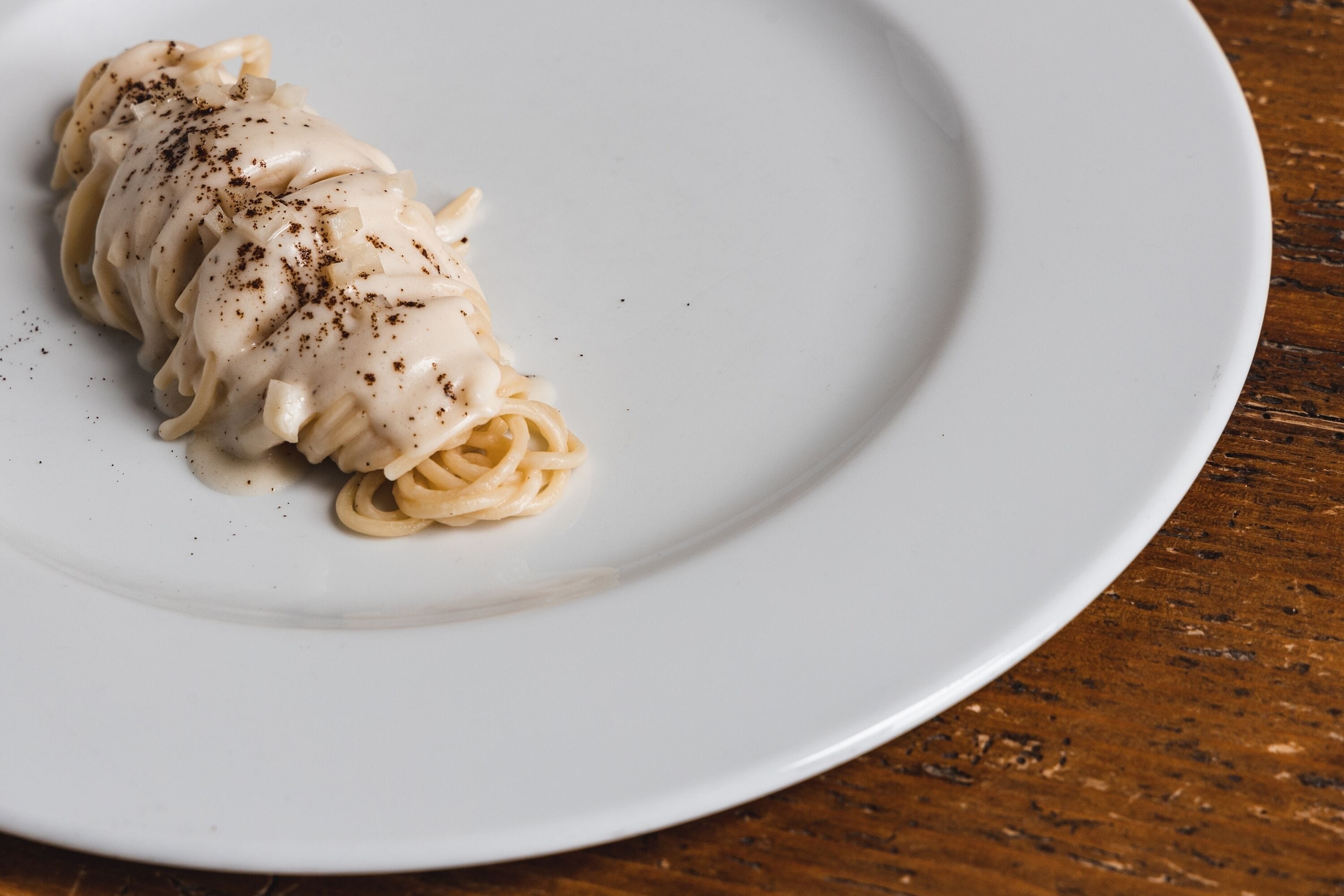 Un plato de pasta con salsa cremosa y pimienta negra sobre un plato blanco.