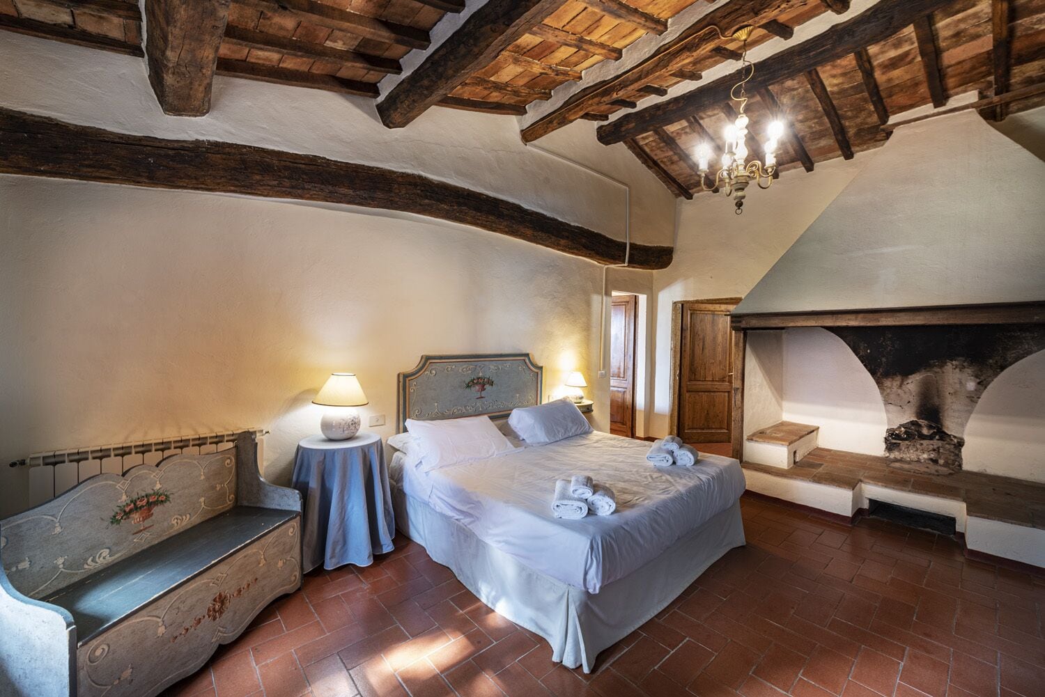 A bedroom with a bed, bedside tables, a bench, and a fireplace.