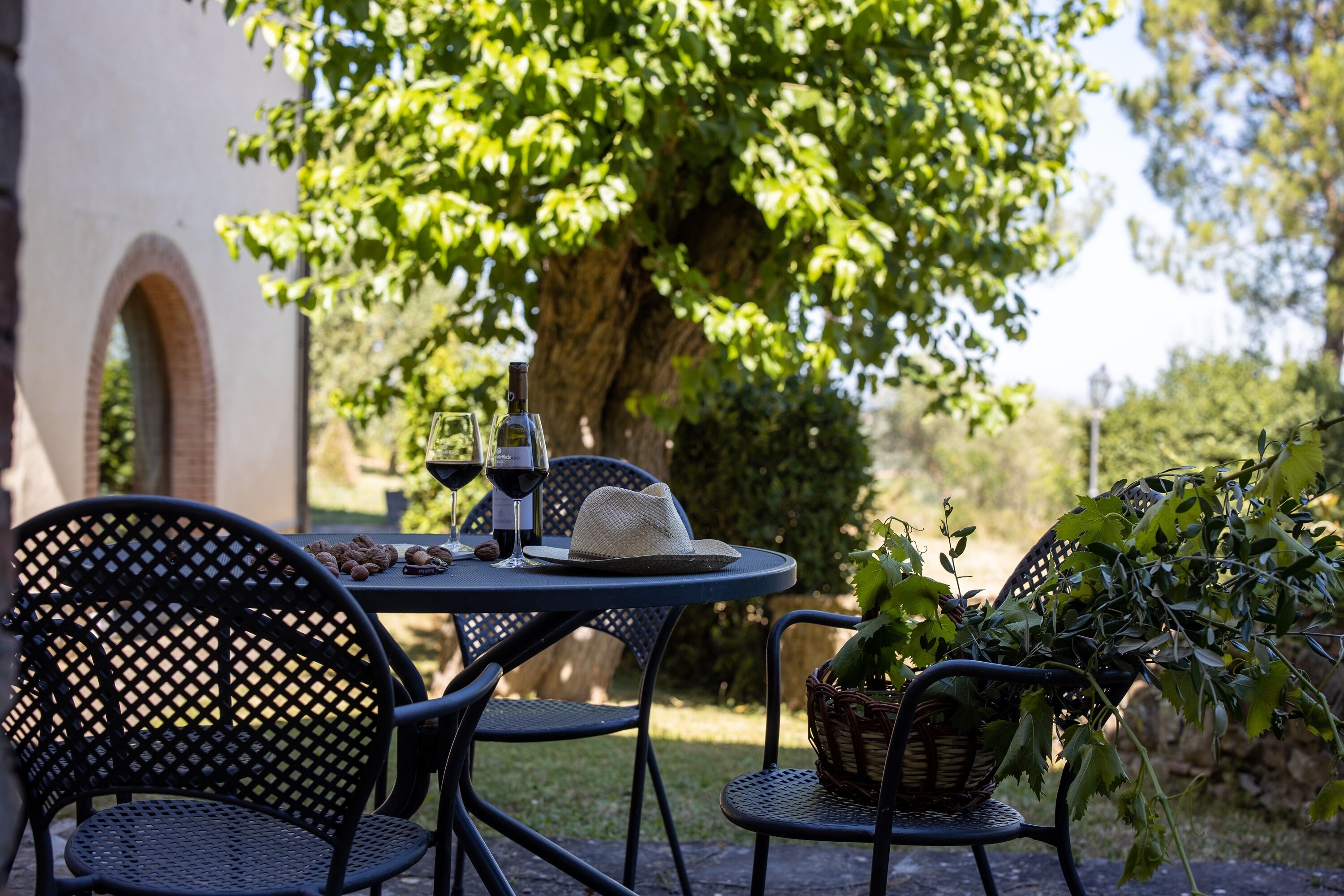 A round table with two chairs, a bottle of wine, a glass, and a basket with a plant.