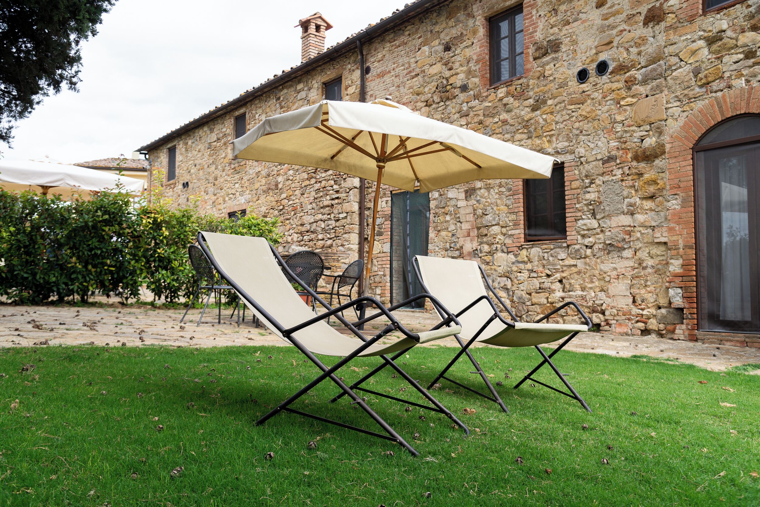 A stone building with a grassy patio, two lounge chairs, and a large umbrella.
