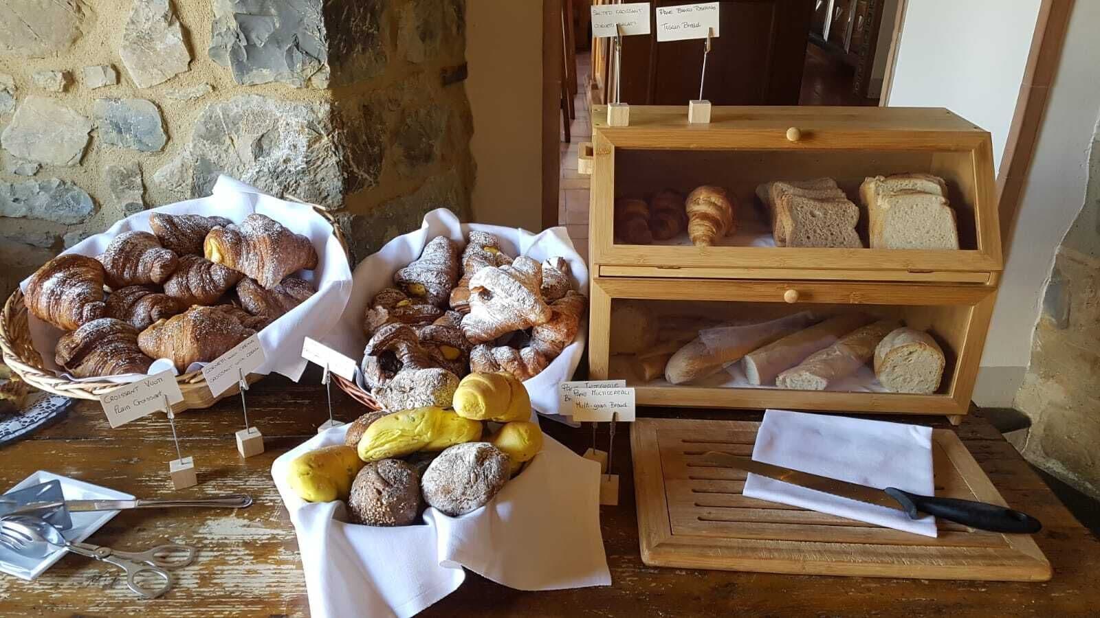 A bakery display with various breads and pastries, including croissants and baguettes, arranged on wooden shelves and in baskets.