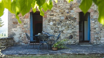Een stenen gebouw met een patio, voorzien van een tafel, stoelen, een plantenmand en uitzicht op het landschap.