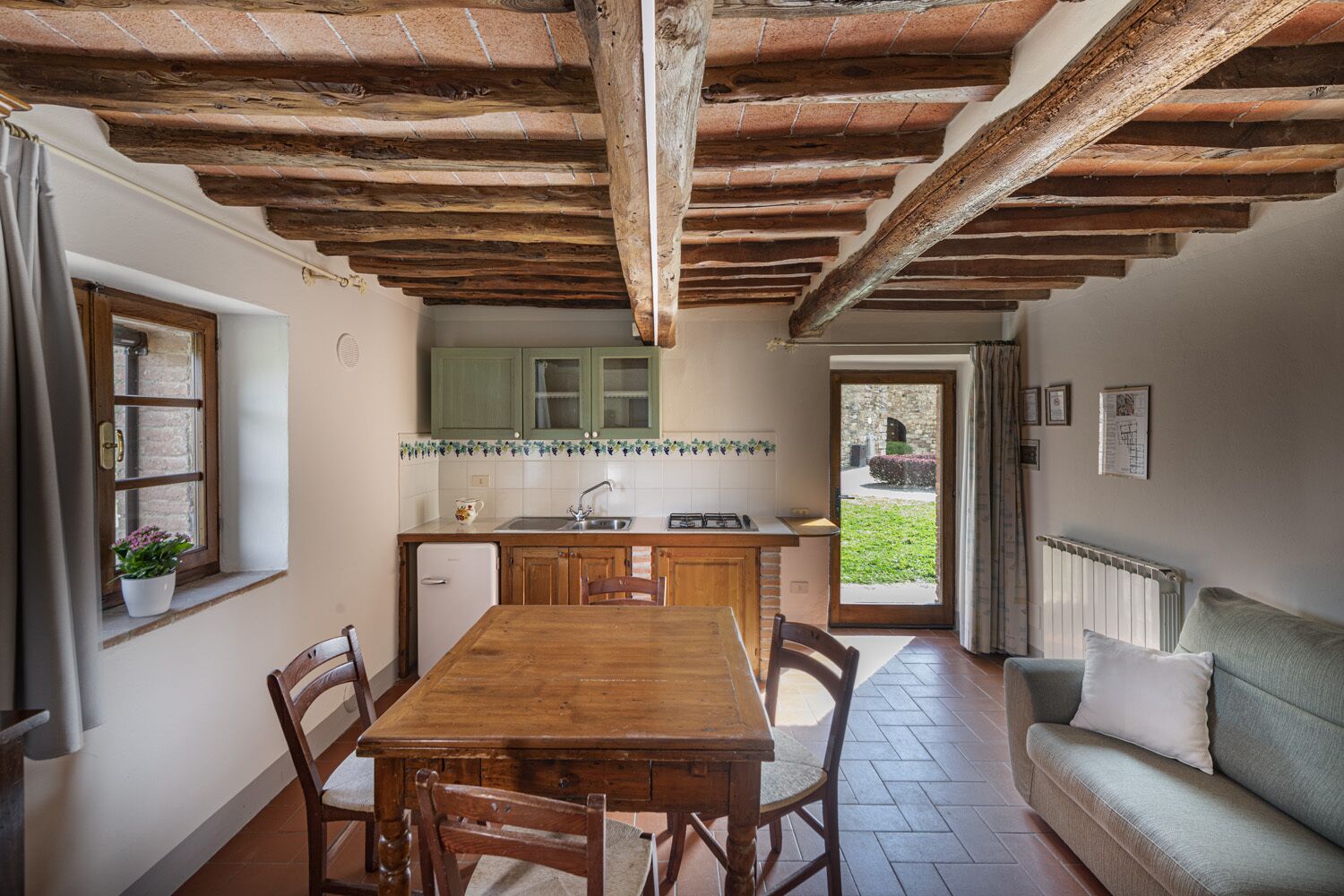 A cozy kitchen with a wooden table and chairs, a small refrigerator, and a window with a plant.