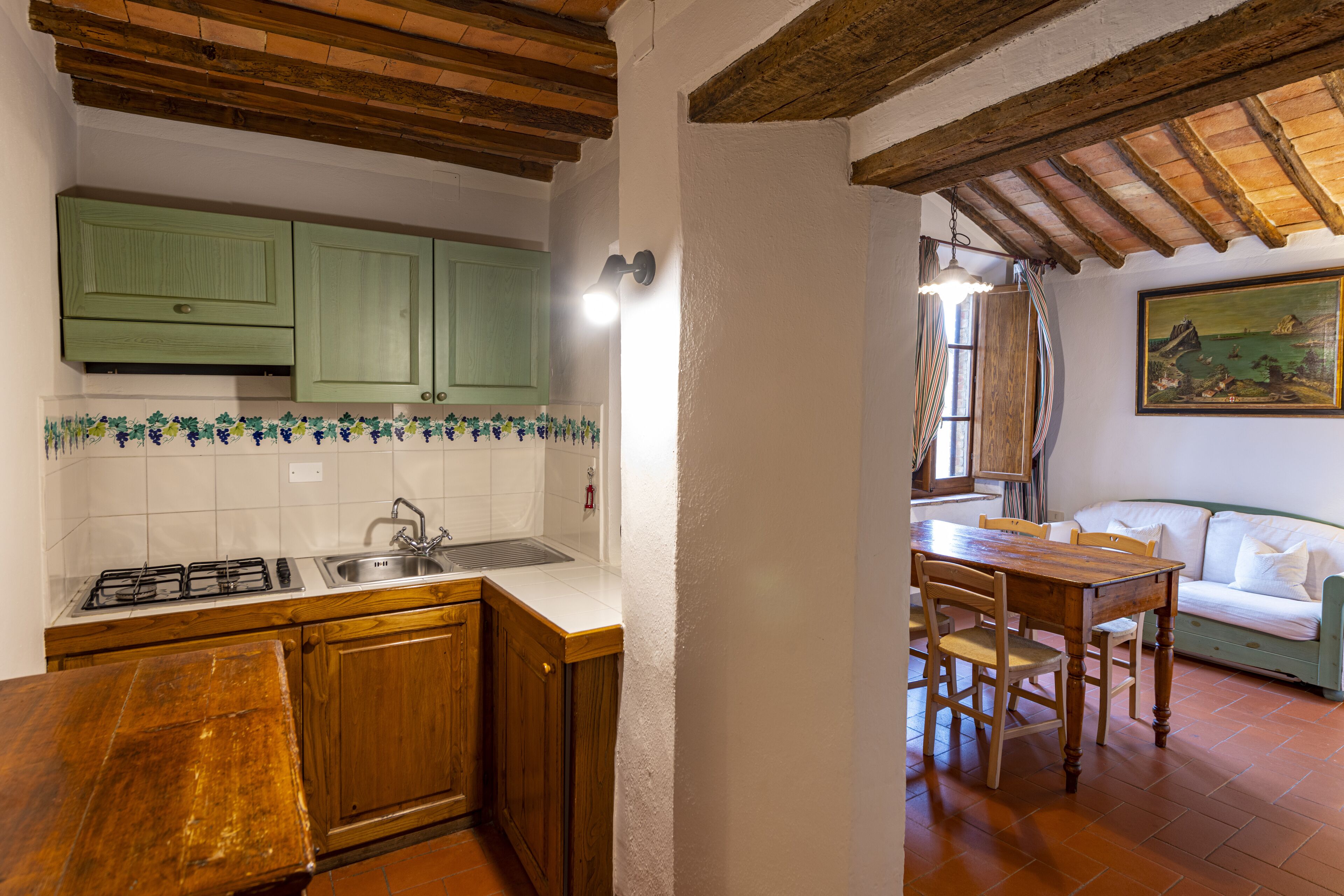 A kitchen with wooden cabinets, a gas stove, and a sink. There is a dining table with chairs in the adjacent room.