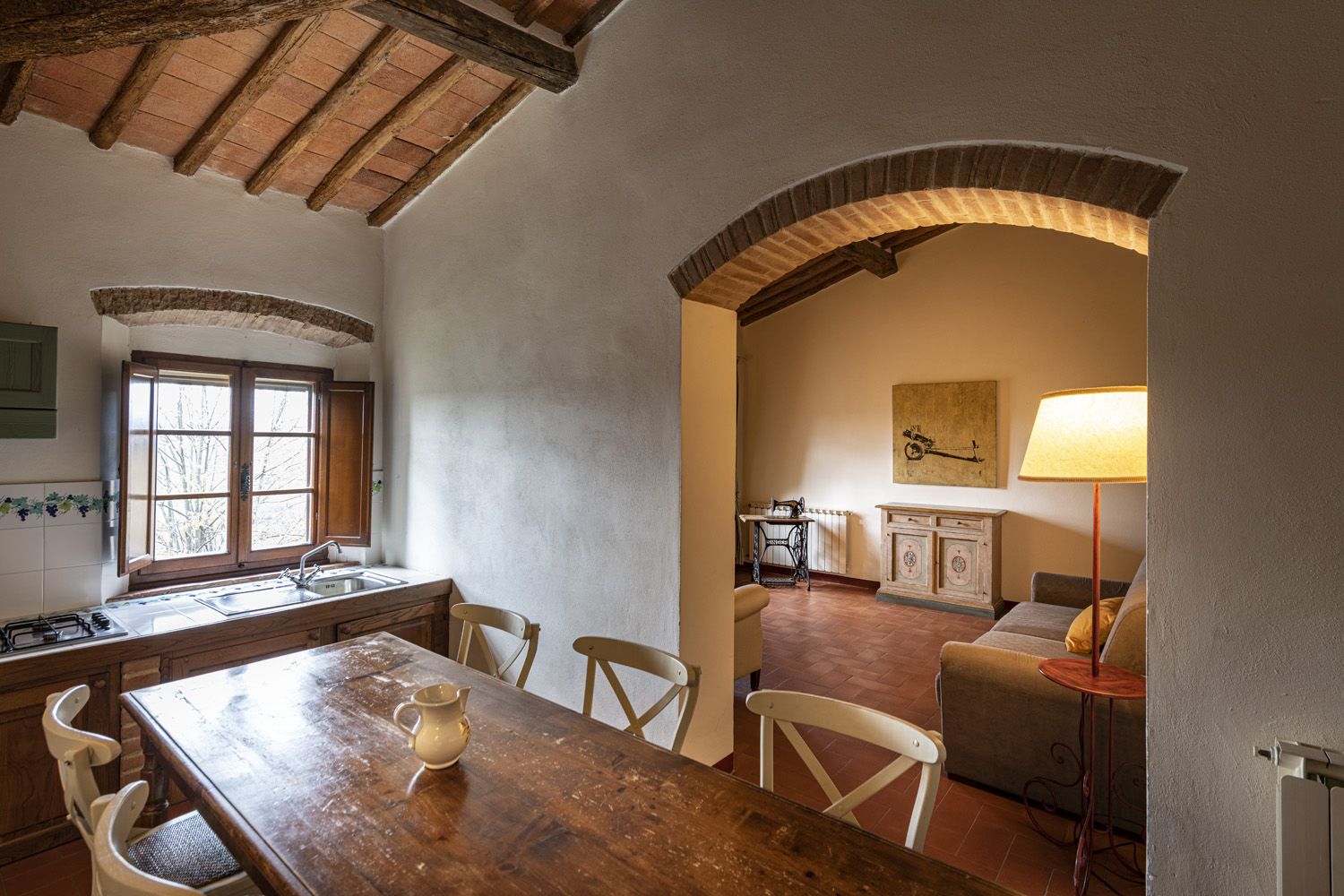 A rustic kitchen with a wooden table, chairs, a sink, and a window.
