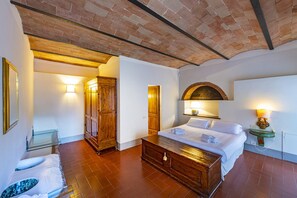 A hotel room with a bed, a wooden cabinet, a glass table, and a bathroom with a shower.
