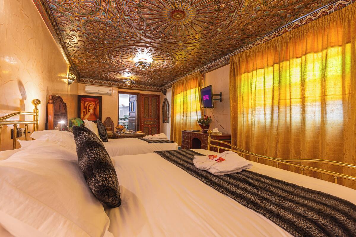A hotel room with two beds, ornate ceiling, and a large window with curtains.