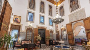 Un intérieur spacieux avec de hauts plafonds, des portes en bois richement décorées et une fontaine centrale.