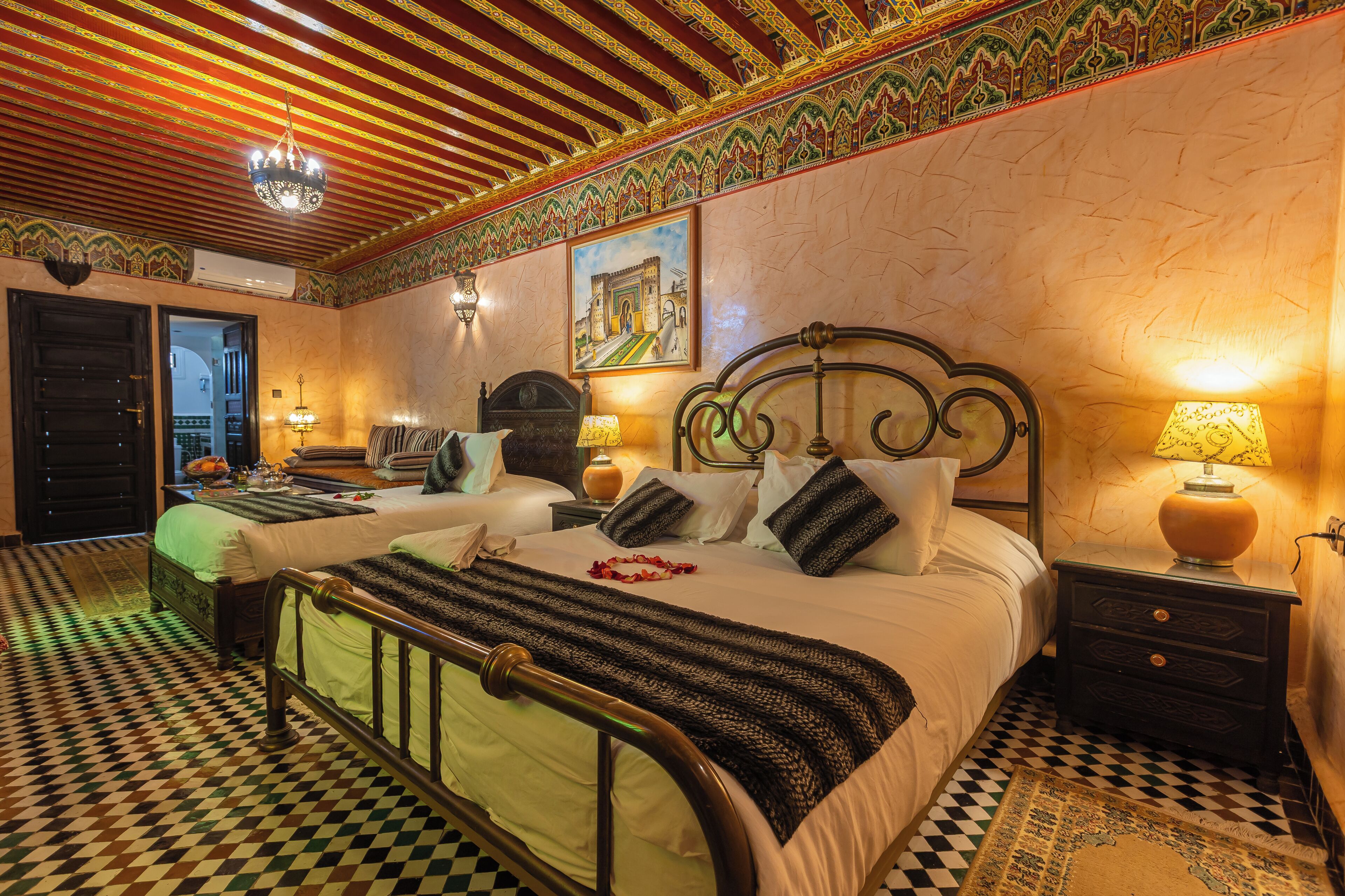 Habitación de hotel con suelo a cuadros, una cama con manta a rayas, dos mesitas de noche con lámparas y un cuadro en la pared.