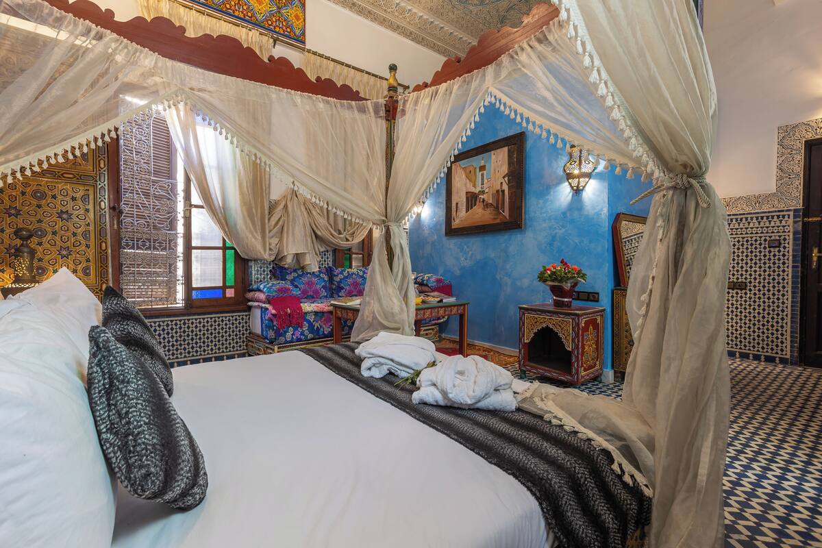A traditional room with a bed, a small table with a lamp, and a wall with a framed picture.