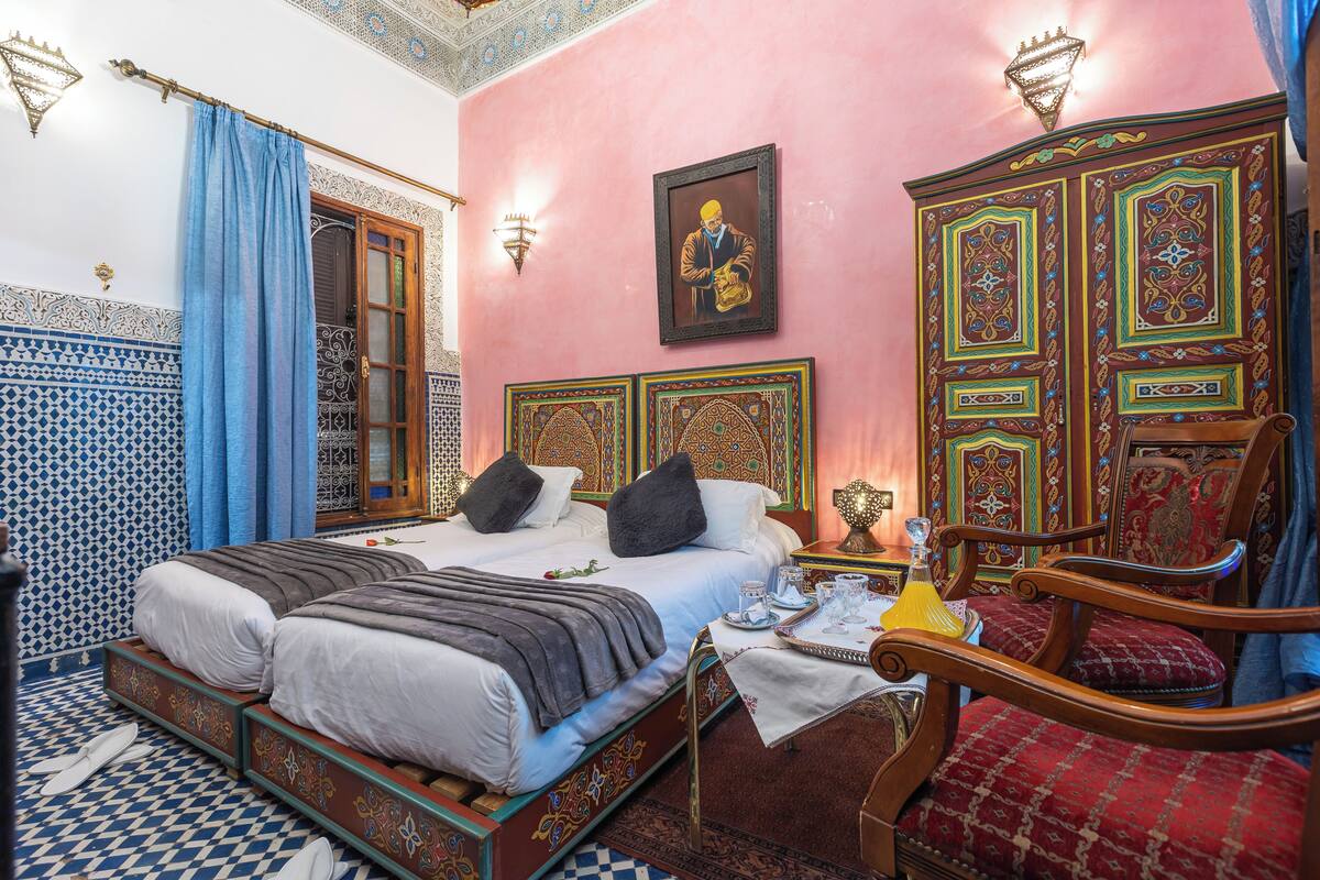 A room with a bed, a chair, a table with a tray, and a wall with a framed picture.
