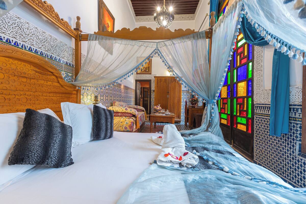 A traditional room with a bed, a wooden headboard, a chandelier, and a colorful stained glass window.