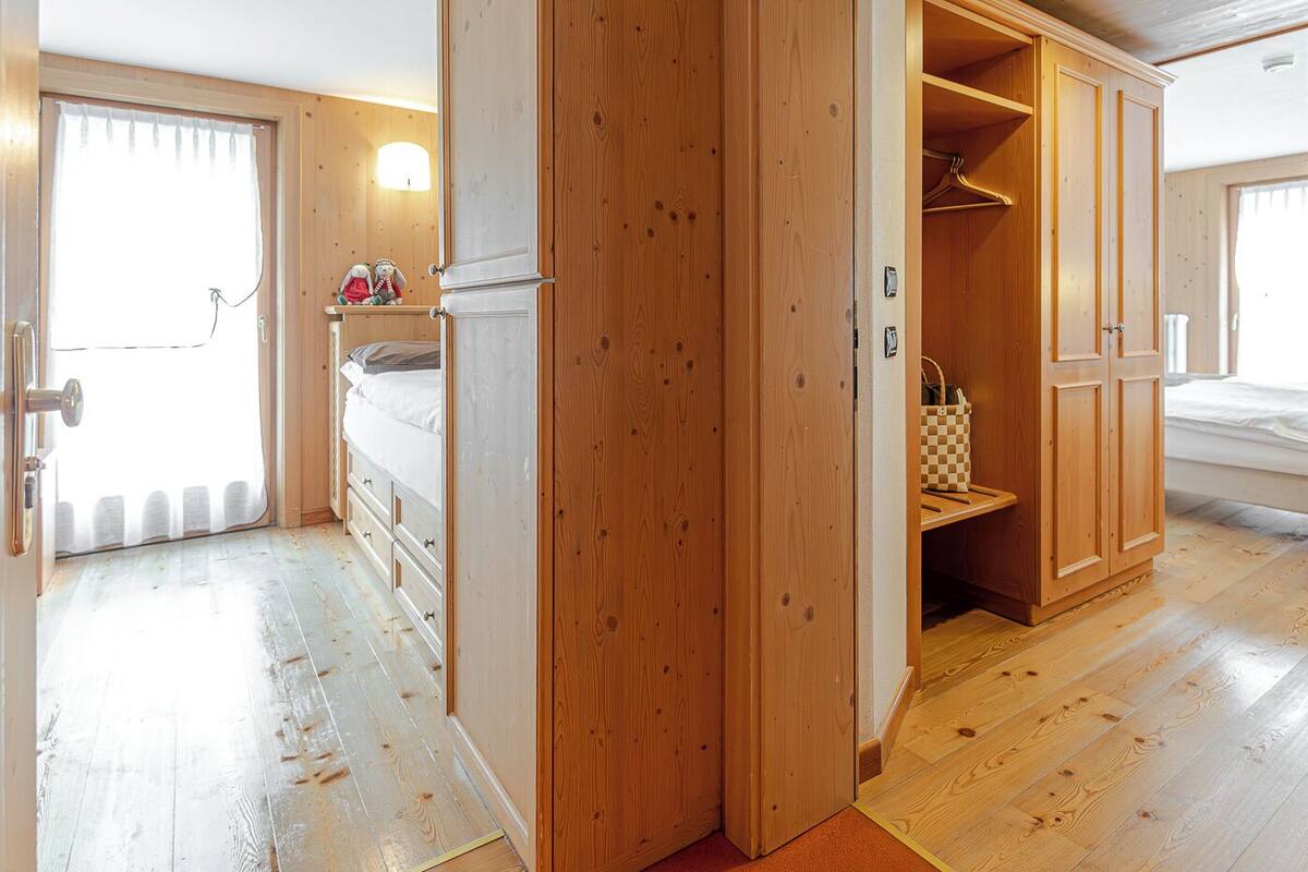 Una habitación con suelo de madera, una cama, un armario y una mesita con un bolso estampado.