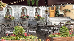An outdoor patio with stone walls, multiple tables and chairs, and hanging flower baskets. - Hotel Pedranzini (Valfurva)