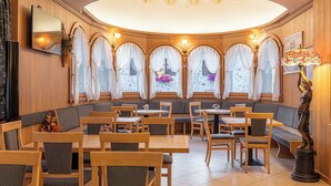 A restaurant with wooden walls, a round table, and a seating area with cushioned benches and chairs. - Hotel Pedranzini (Valfurva)