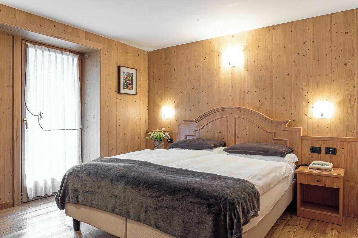 Un dormitorio con cabecera de madera, una mesita de noche con lámpara y una ventana con cortinas.