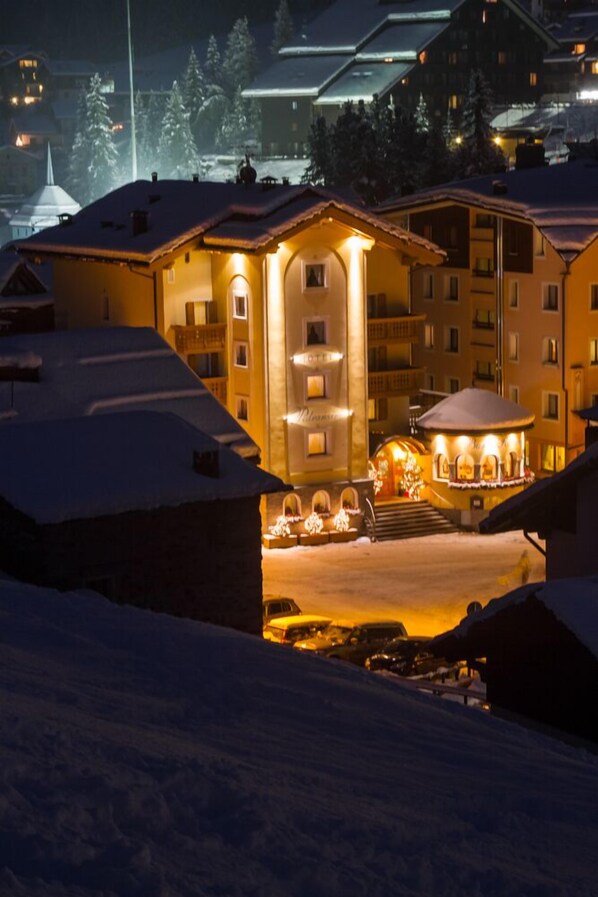A snow-covered building with multiple balconies and a central illuminated area, likely a lobby or common space. - Hotel Pedranzini (Valfurva)