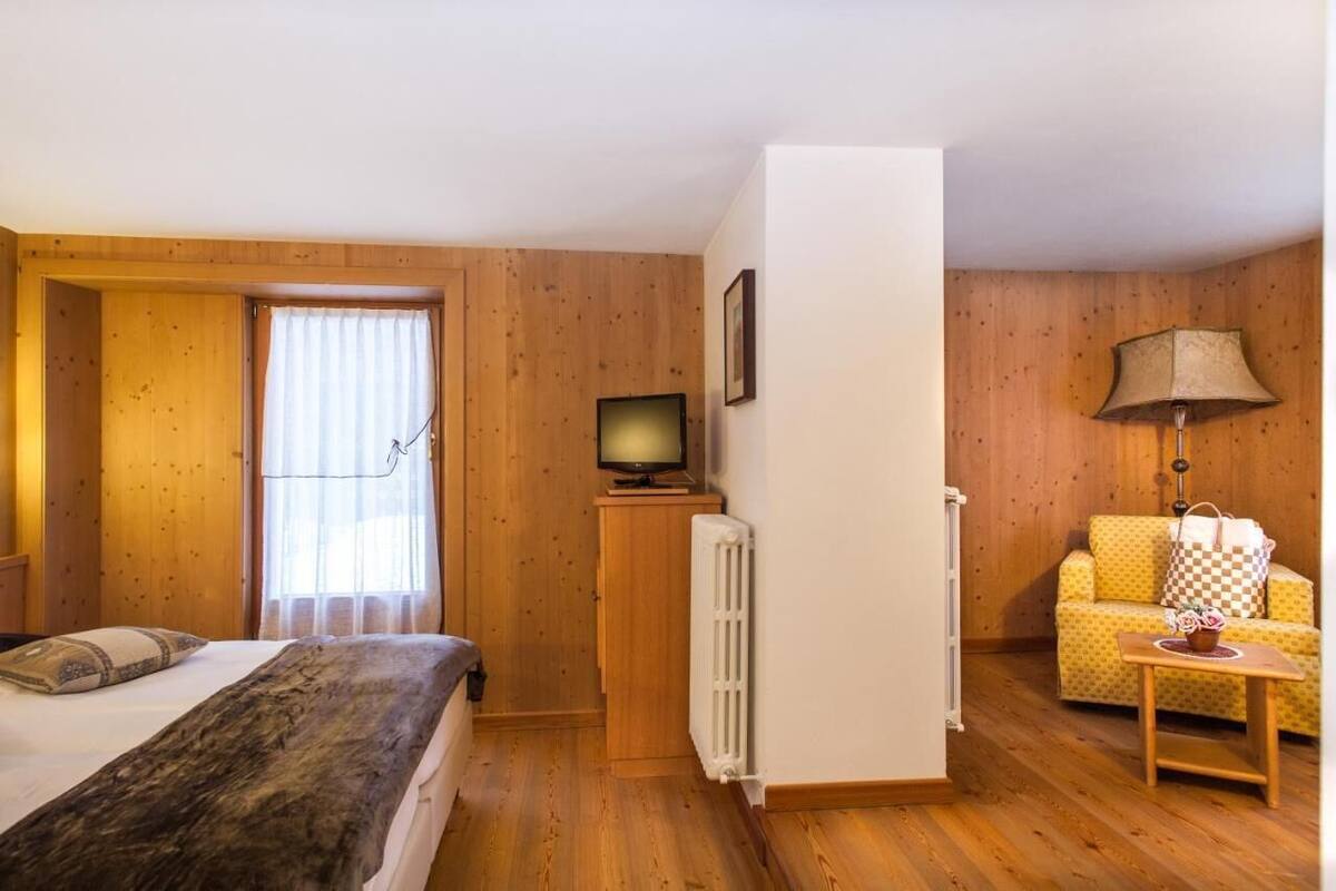 Una habitación acogedora con una cama, un televisor sobre un mueble, un radiador, un sofá y una lámpara.