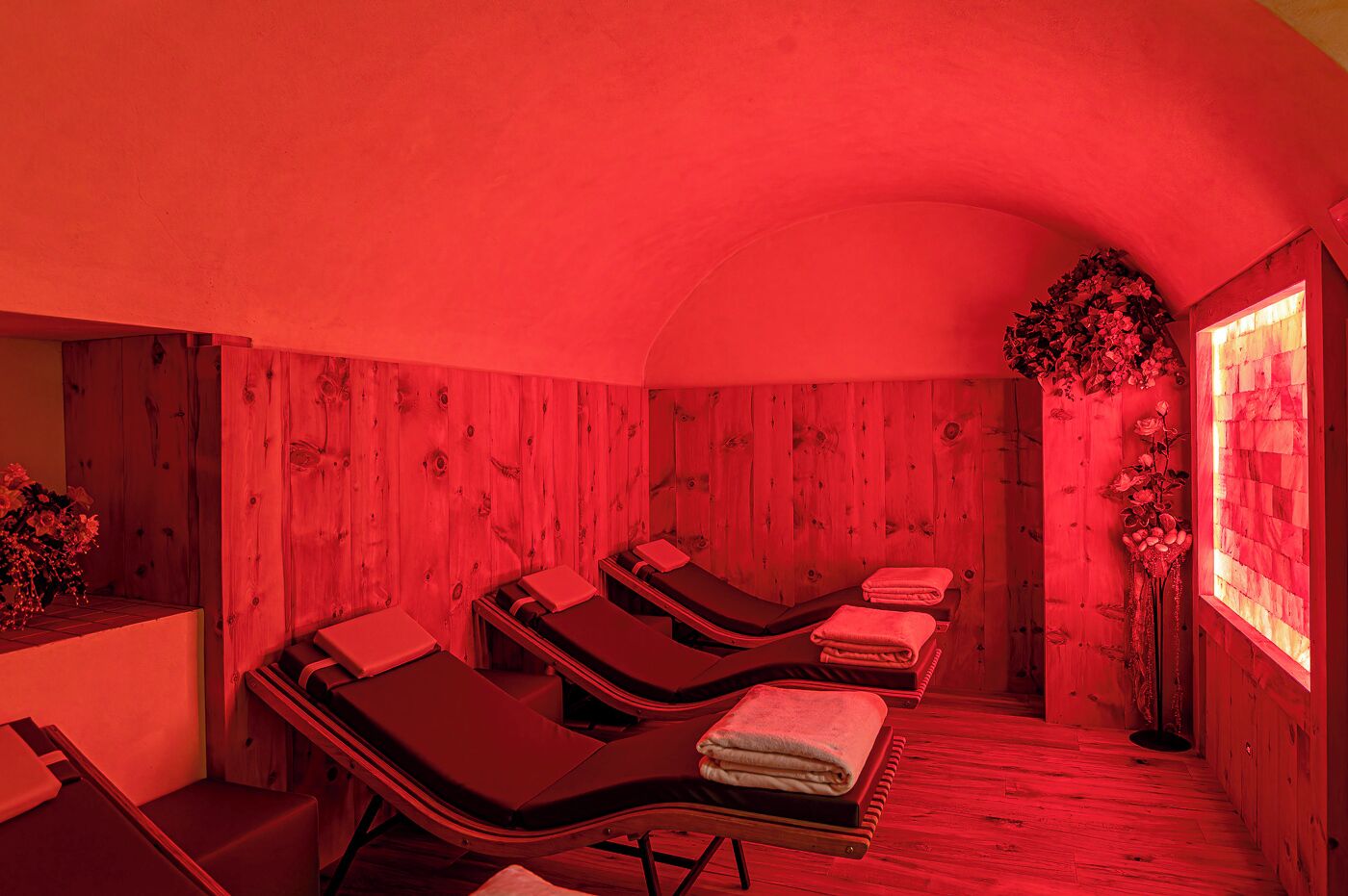 A red-lit room with wooden walls, three reclining chairs, and a window with a view of the outside.