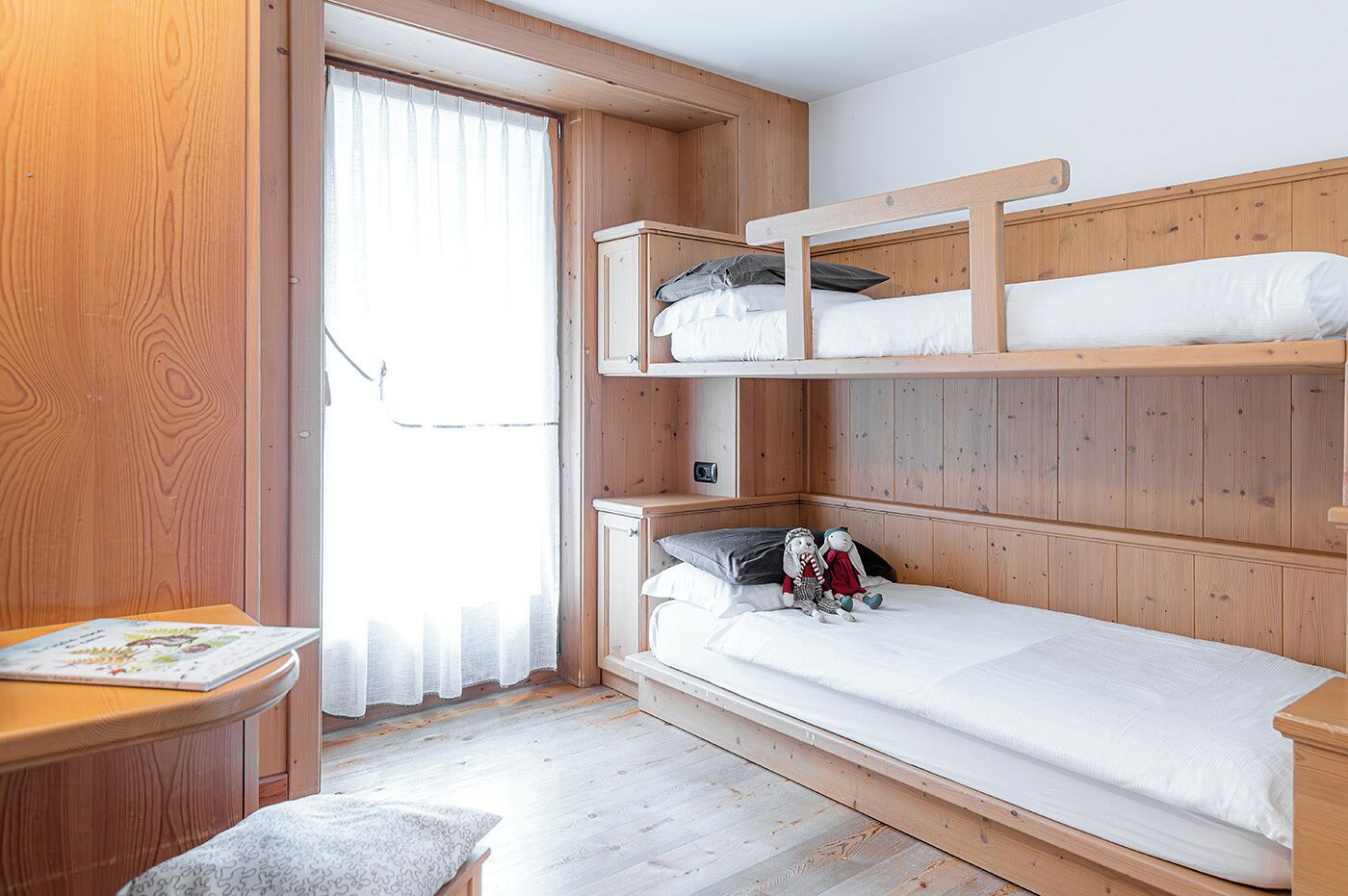 A wooden bunk bed room with a desk and a window.