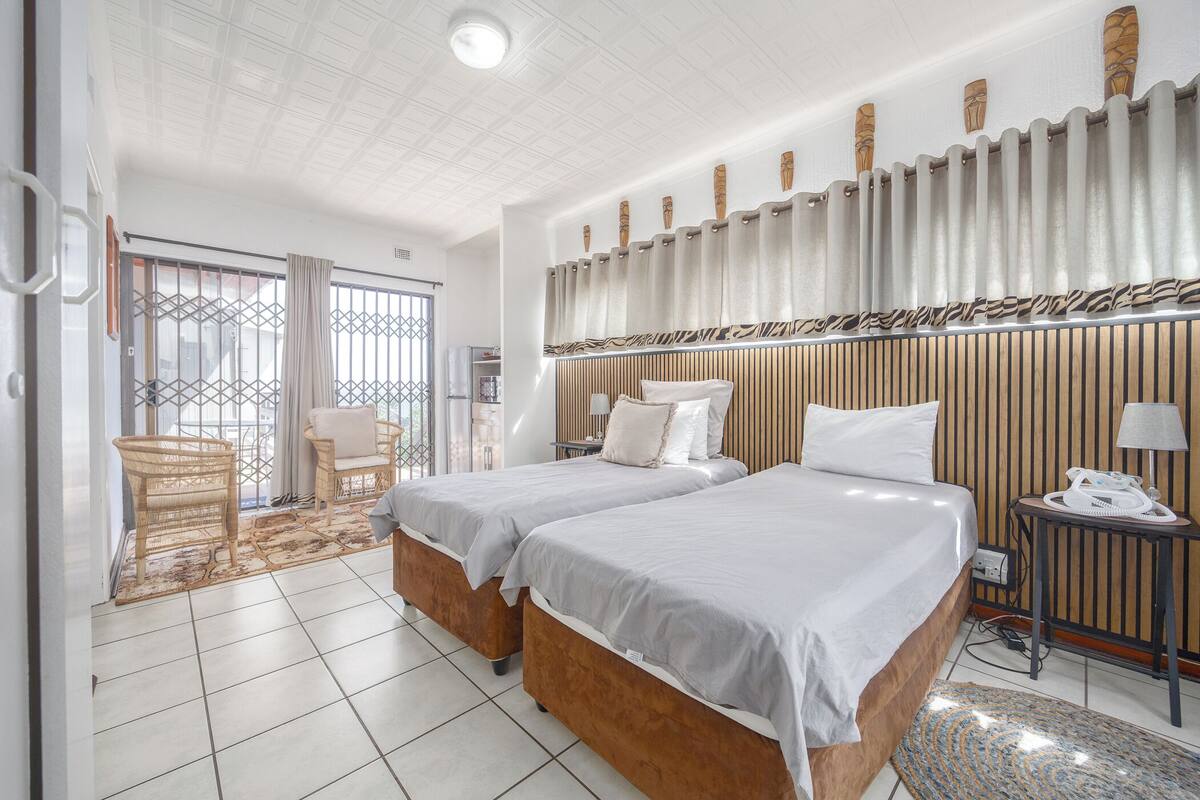 A hotel room with two beds, a wooden headboard, a telephone, and a small table with a lamp.