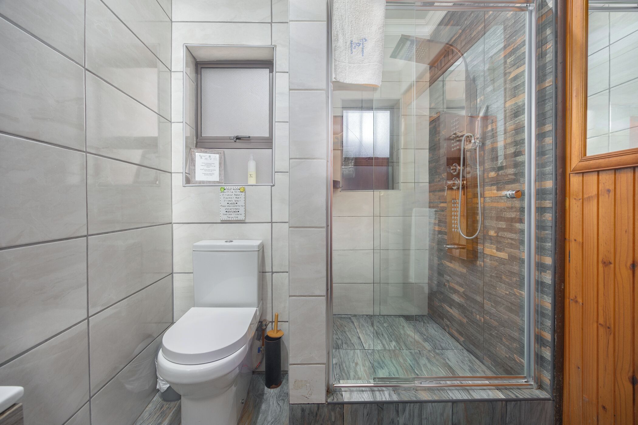 A modern bathroom with a toilet, a glass shower enclosure, and a wooden door.