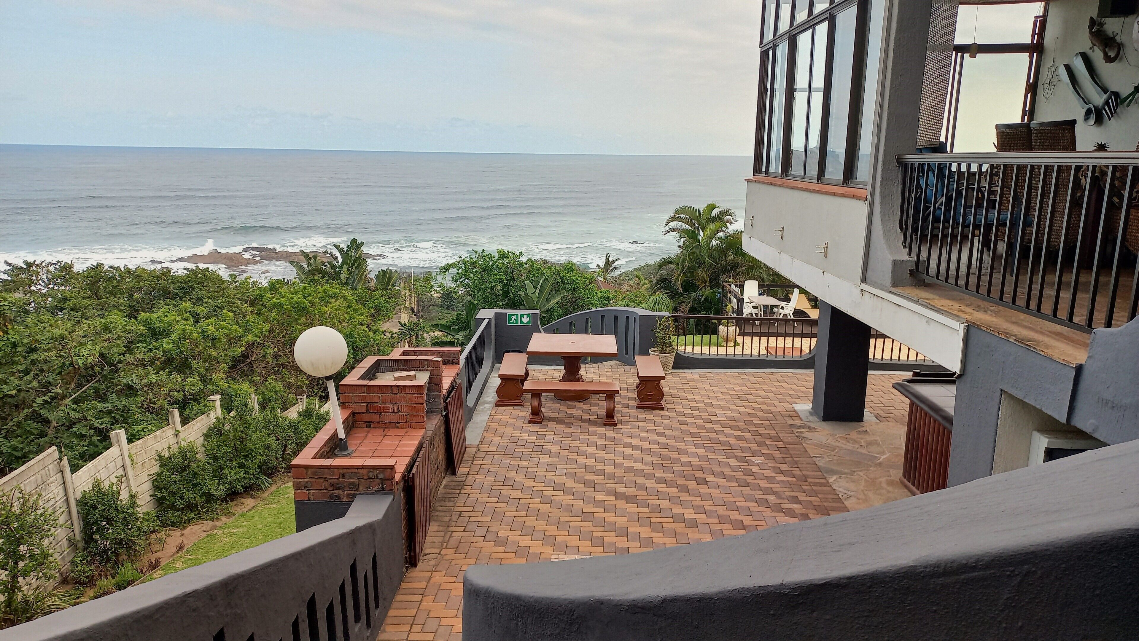 Pátio com piso de tijolos, uma mesa e bancos com vista para o oceano.