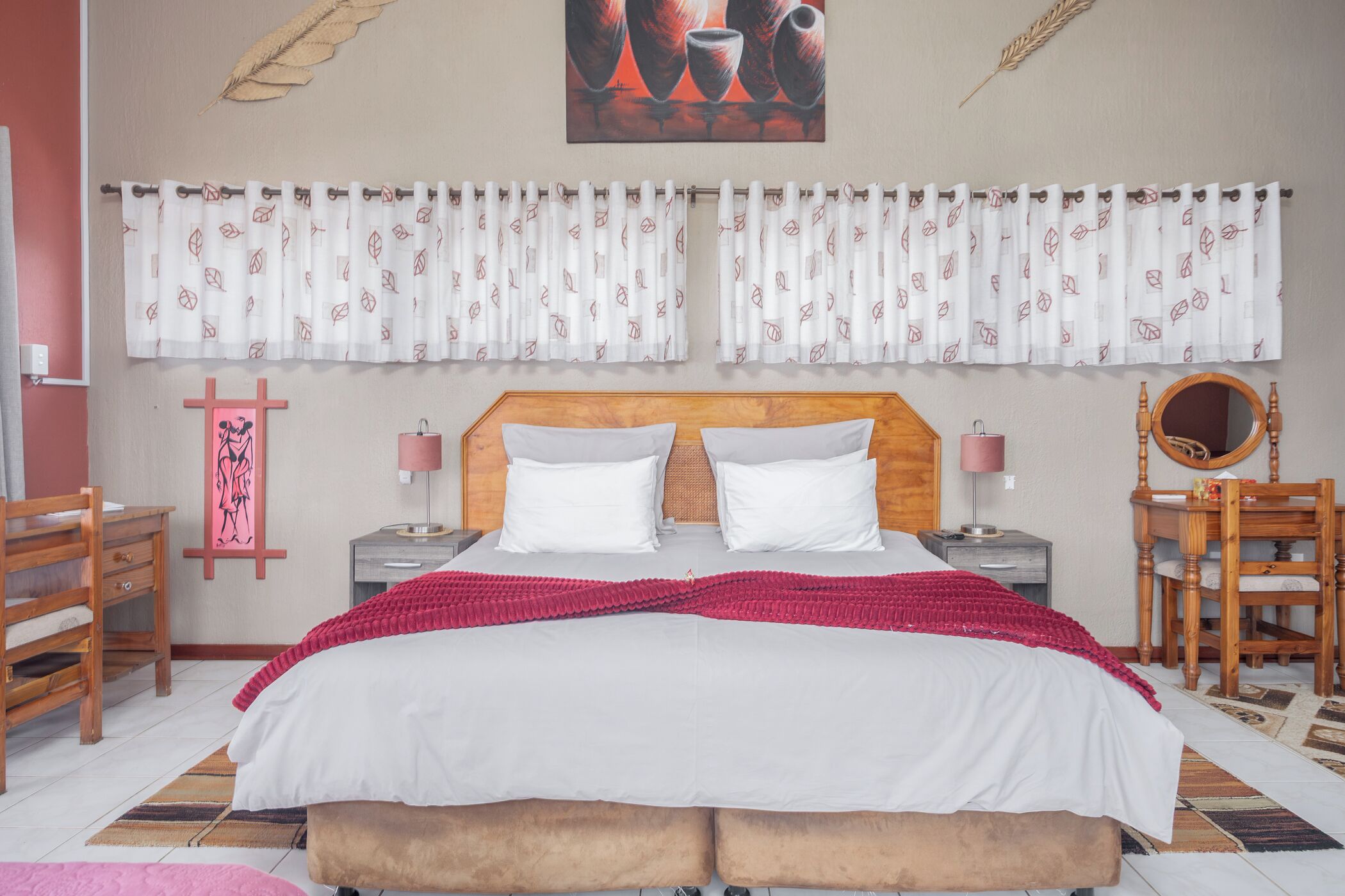 A bedroom with a large bed, two bedside tables, a wooden headboard, a mirror, a chair, and a wall-mounted artwork.