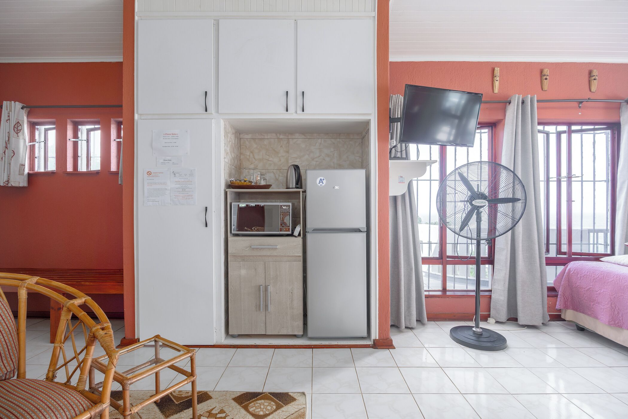 Una habitación pequeña con kitchenette, una cama, un ventilador y televisión.