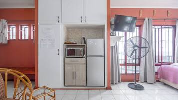 Una habitación pequeña con kitchenette, una cama, un ventilador y televisión.