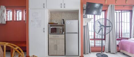 Une petite pièce comprenant un coin cuisine, un lit, un ventilateur et un téléviseur.