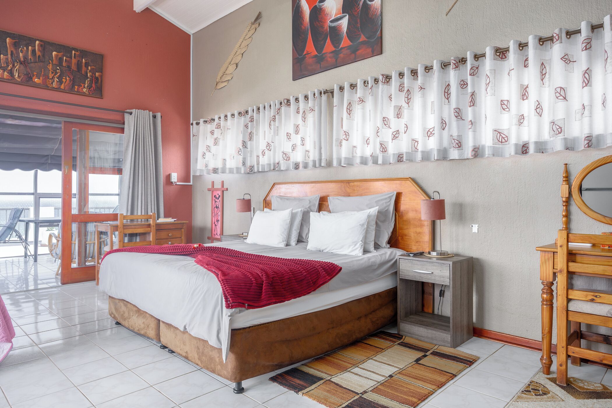 A bedroom with a large bed, a wooden nightstand, a desk, and a chair.