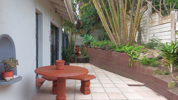 A patio with a round table and chairs, surrounded by a brick wall with plants and a statue.