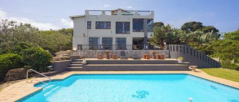A modern two-story house with a swimming pool in front.