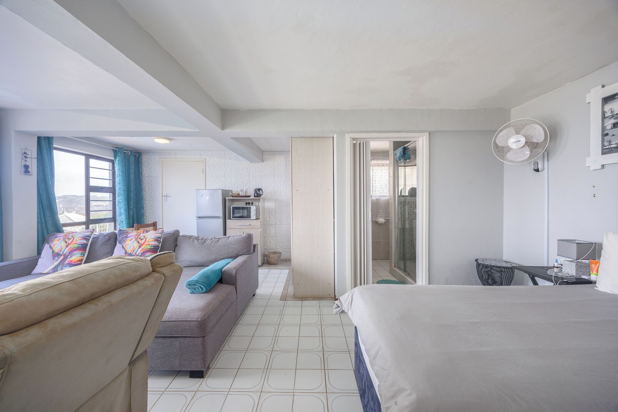 A modern hotel room with a bed, sofa, and a small kitchenette.