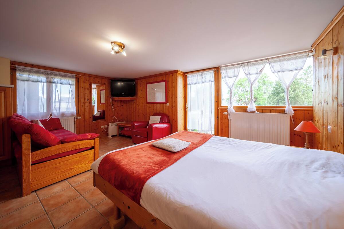 A cozy room with a wooden bed, a red sofa, a small desk, and a television.