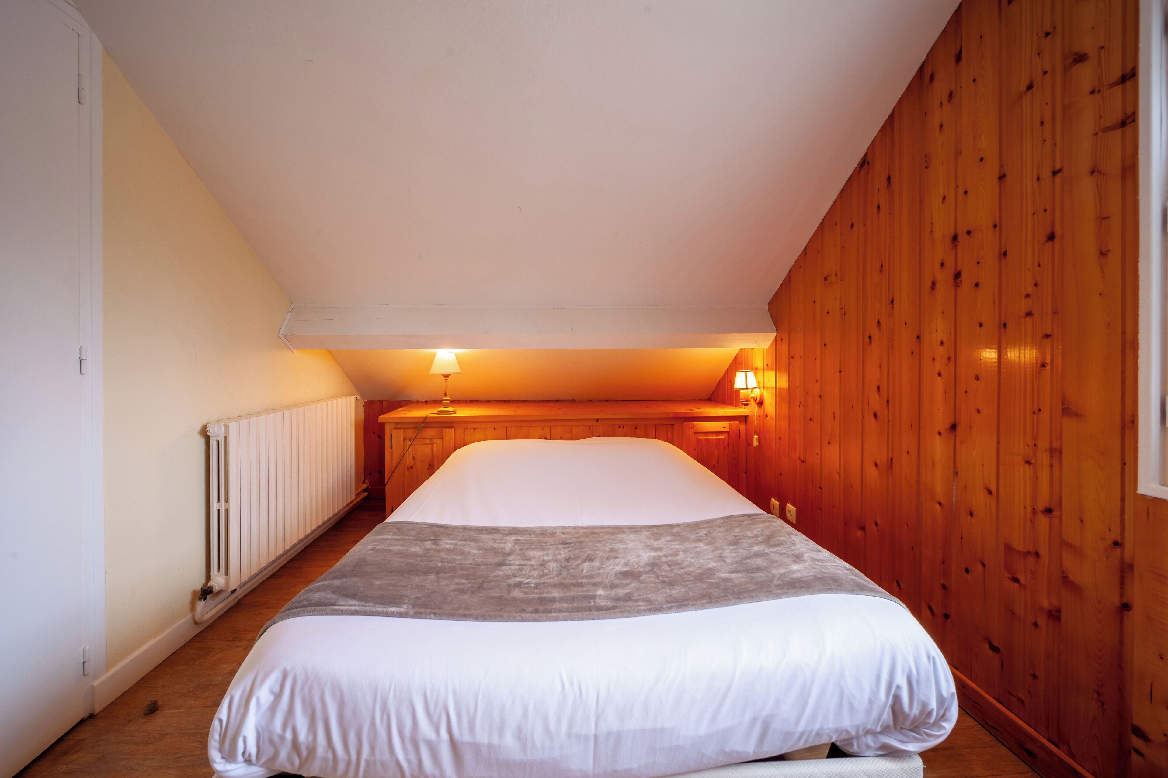 Een slaapkamer met een groot bed, houten wanden, een radiator en twee wandlampen.