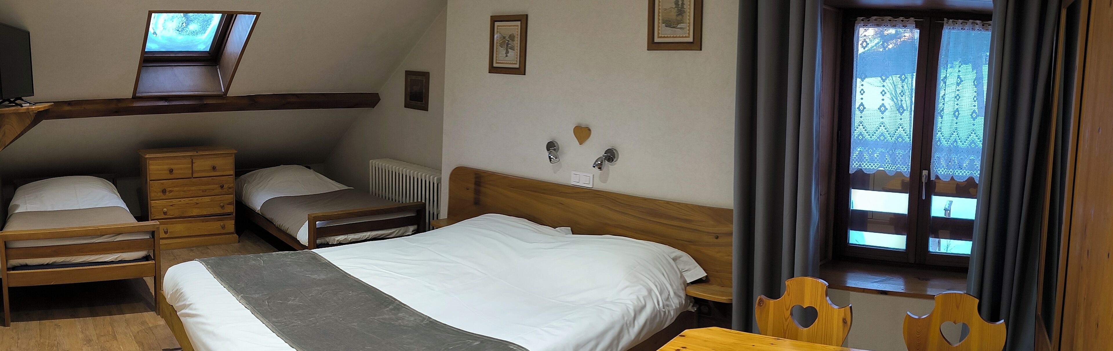 A bedroom with a bed, a desk, a chair, a dresser, and a window with curtains.