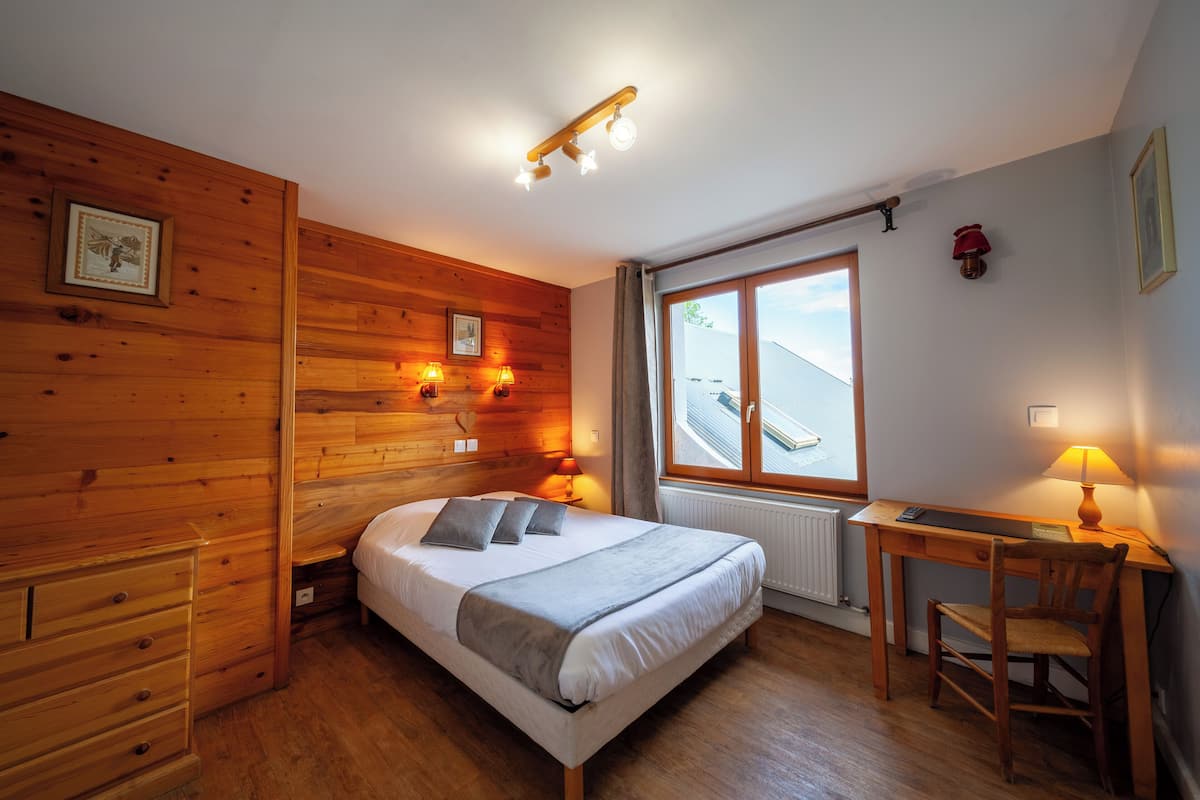 A wooden-paneled bedroom with a bed, bedside lamps, a desk, and a chair.