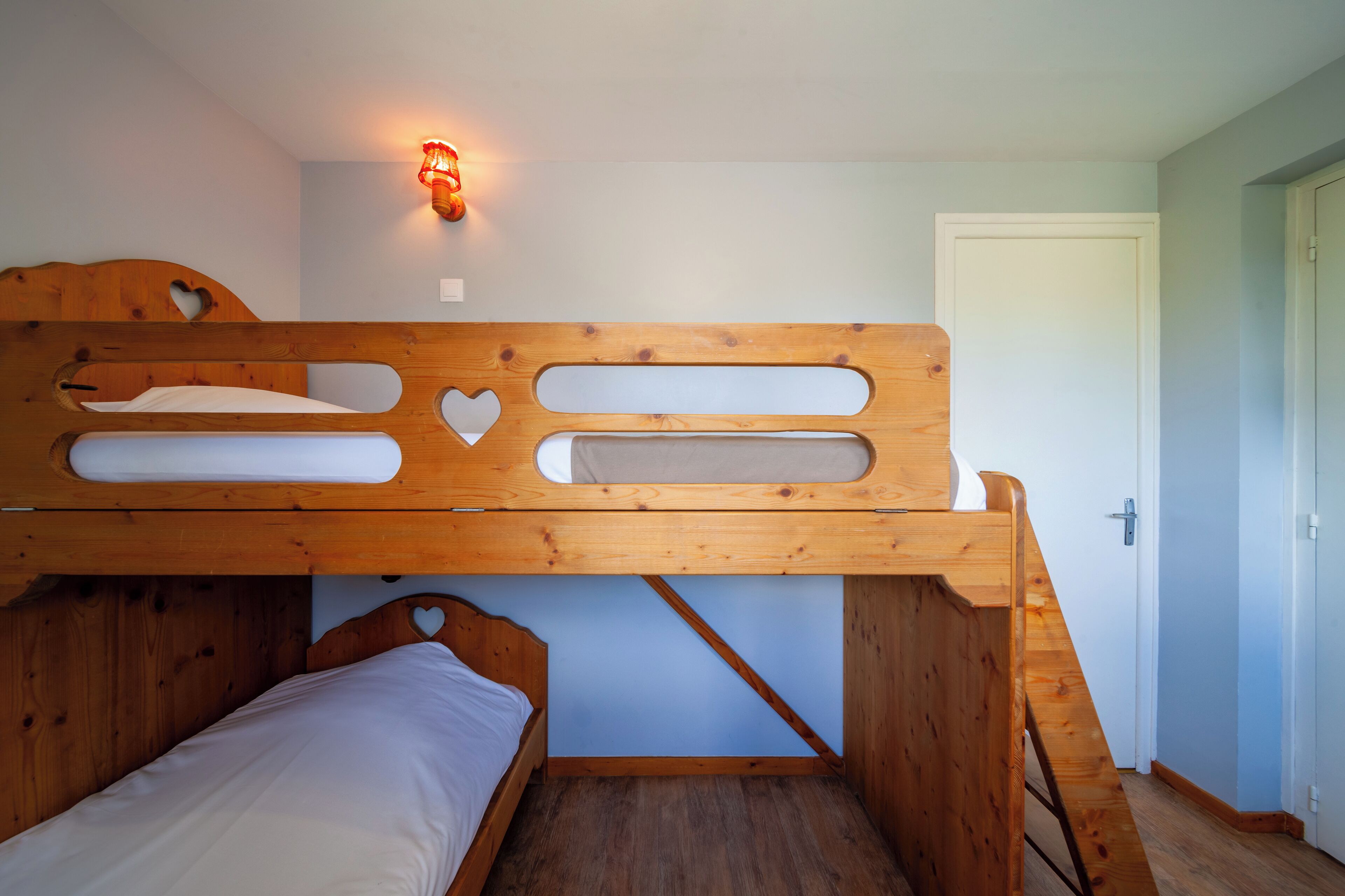 A bunk bed with a wooden frame, a small window, and a wall-mounted light fixture.