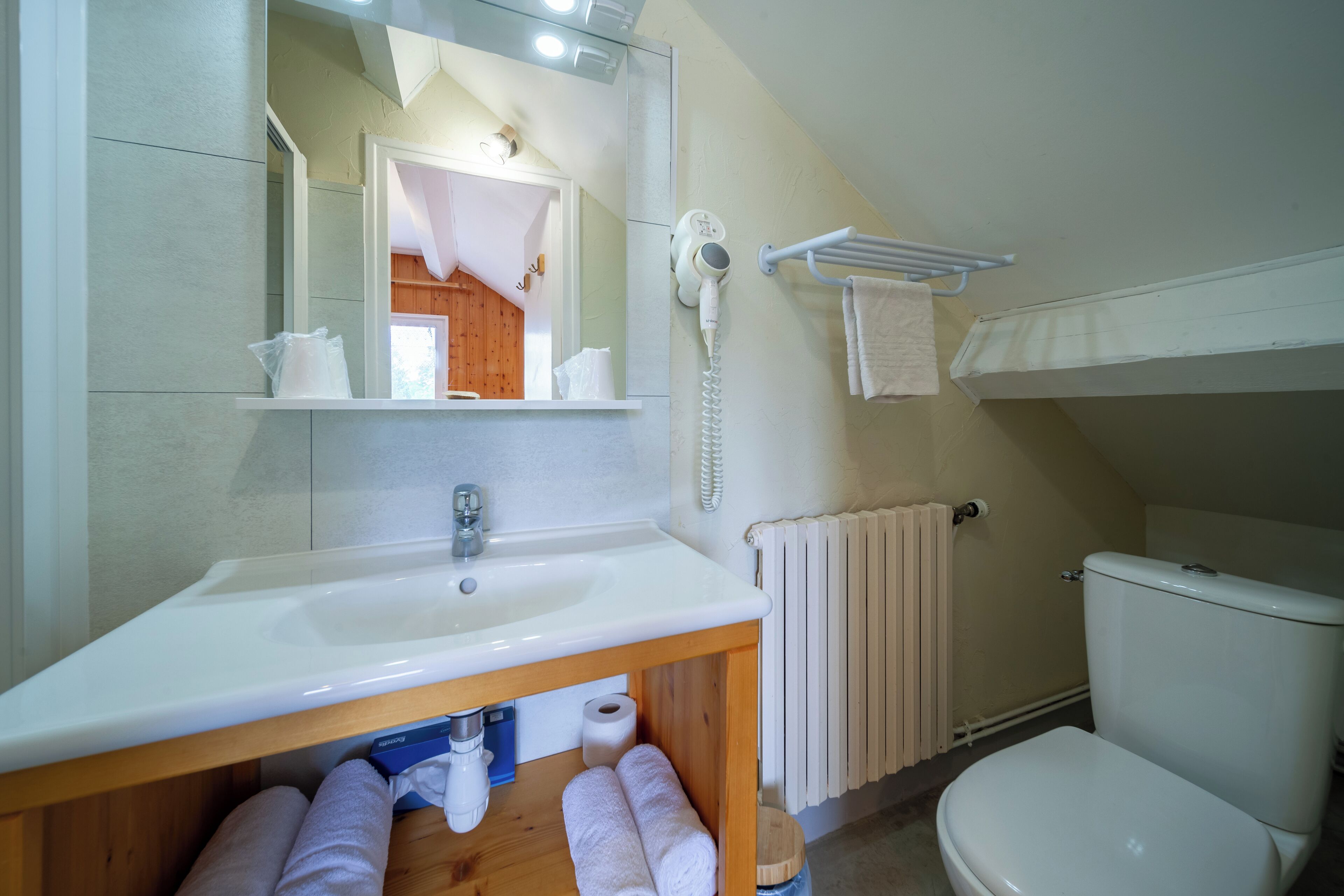 Un baño con lavamanos blanco, espejo, secador de pelo, toallero y retrete.