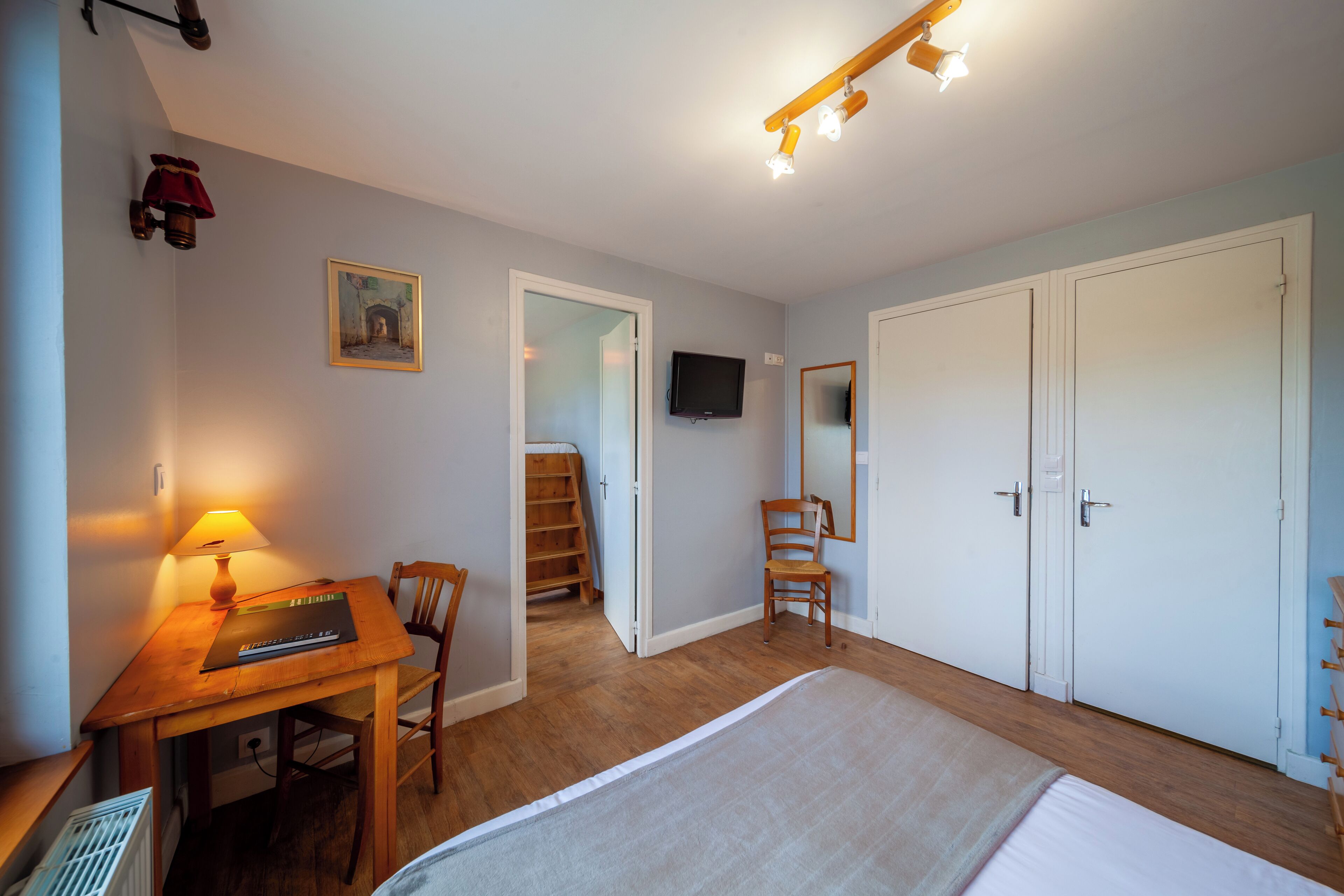 Ein Schlafzimmer mit Bett, Schreibtisch mit Lampe, Stuhl, Fernseher und Kleiderschrank.