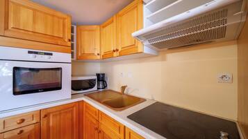 A compact kitchen with wooden cabinets, a built-in microwave, an oven, a sink, and a stovetop.