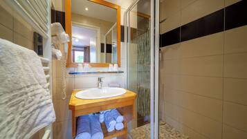 Un baño moderno con tocador de madera, lavamanos blanco y cabina de ducha de vidrio.