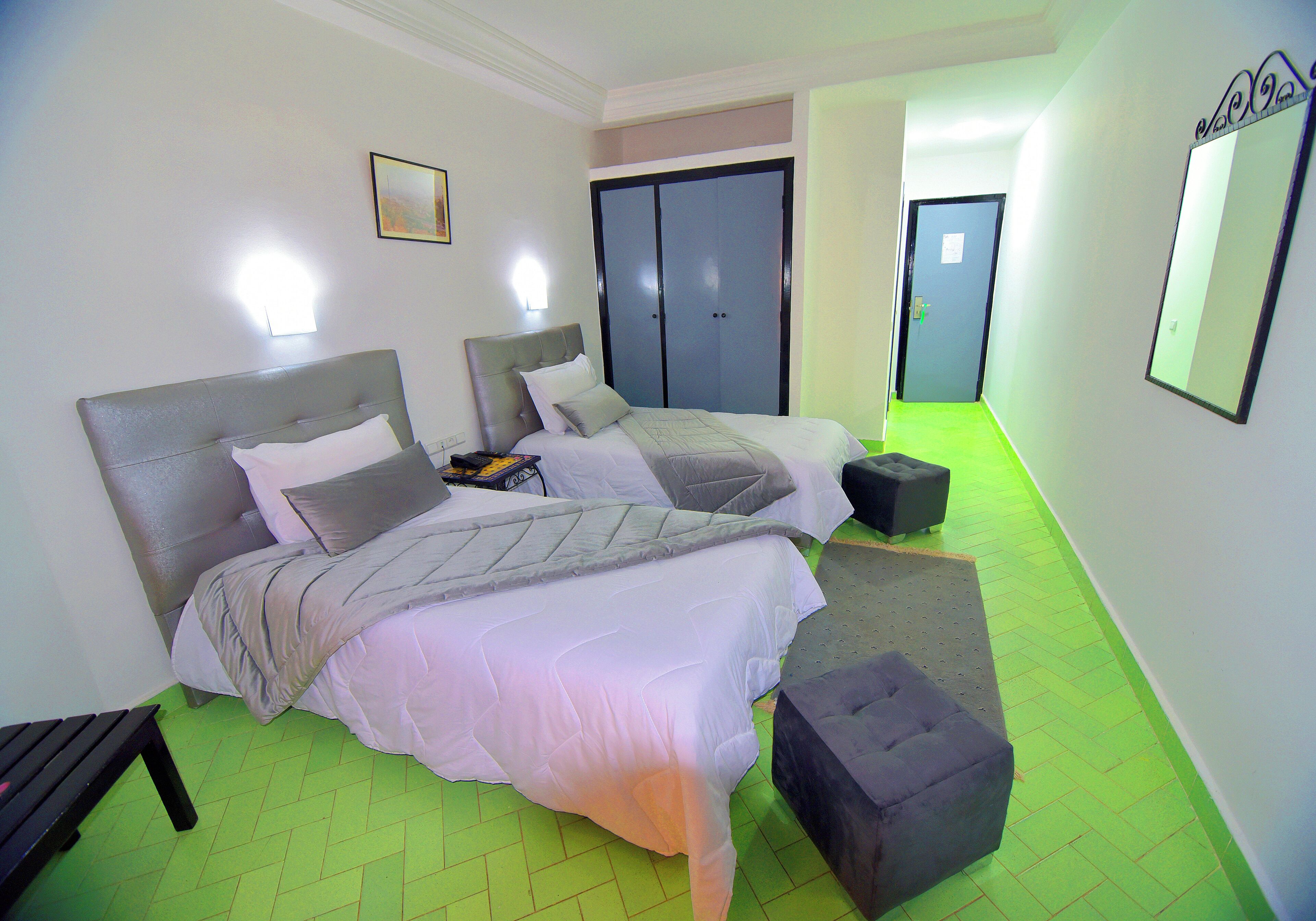 Een hotelkamer met twee bedden, een grijze hoofdbord, een grijze bank en een groene visgraatvloer.