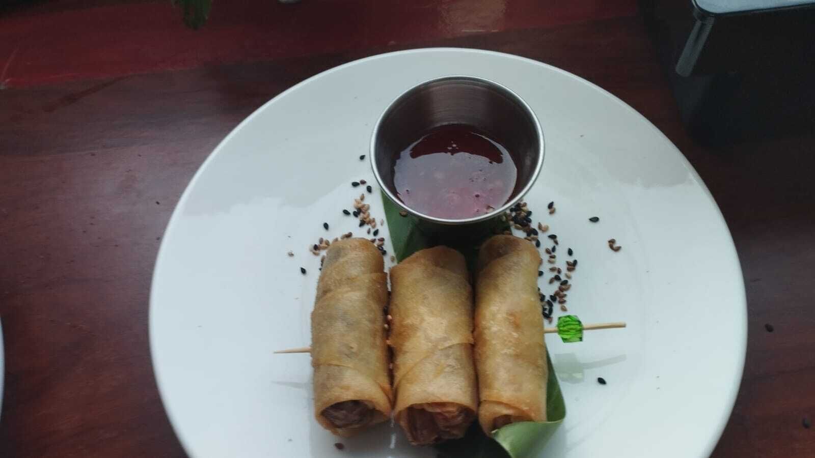 A plate with three spring rolls and a small bowl of dipping sauce.