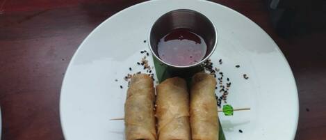 A plate with three spring rolls and a small bowl of dipping sauce.