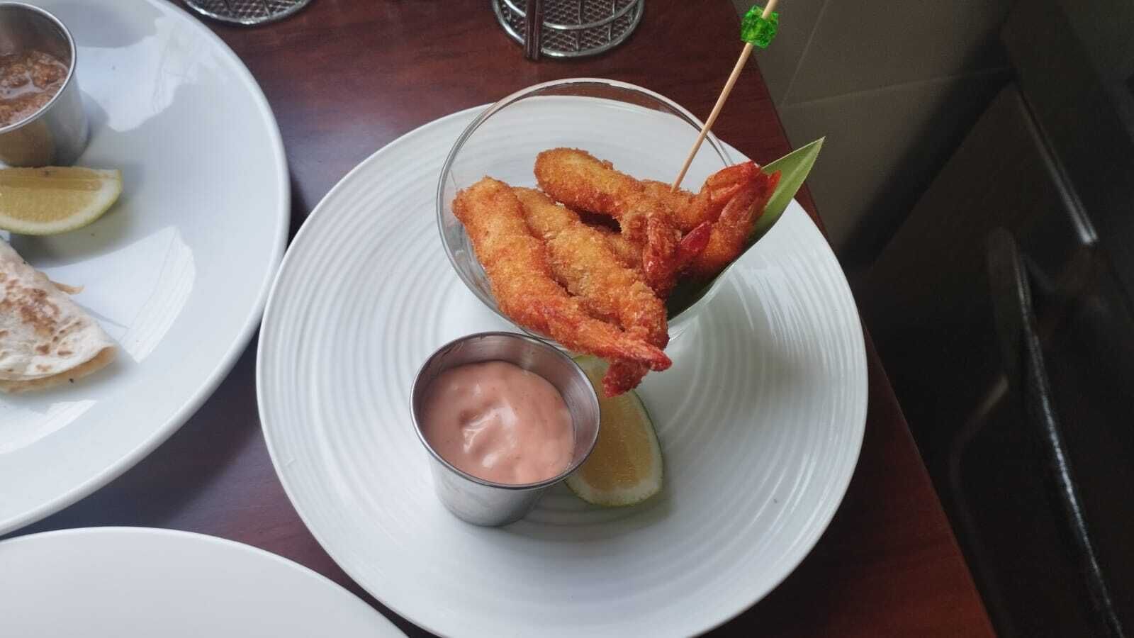 A plate with fried food, a small cup of sauce, and a slice of lemon.